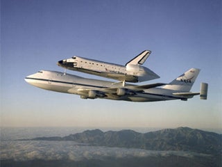 A photo of the Space Shuttle Atlantis, attached to the top of a Boeing 747 in flight for relocation.