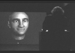  A black and white photo of a computer-rendered head projected on a screen.