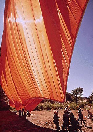 A tremendous orange cloth being hoisted into the air by teams of workers.