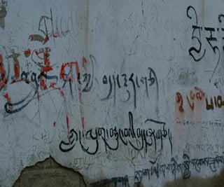 Tibetan graffiti on a crumbling plaster wall.