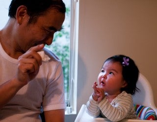 An infant in a high chair focuses her attention on a man sitting next to her.