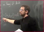 A men standing in front of a blackboard and pointing the blackboard with right hand.