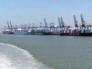 Row of container ships in dock with cranes overhead.