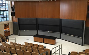 8 rows of fixed furniture tablet arm chairs facing blackboards and a rectangle table.