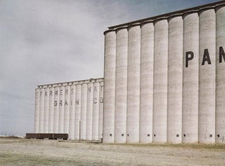 A photo of two rows of tall concrete grain elevators with a few railroad cars.