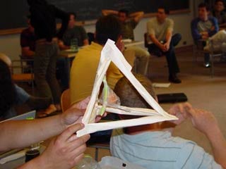 A photograph of a student-constructed egg protection device.  The device consists of a paper pyramid with an egg suspended within. 