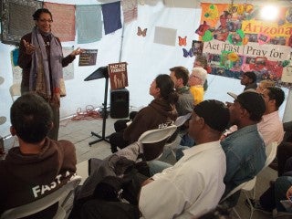 An African-American woman smiles and gestures as she addresses a diverse group of listeners.