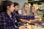 A photo of a group of girls working around a laptop.