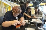 A photo of a group of girls sitting at a table, working on building cameras.