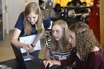 A photo of three girls working together at a laptop.