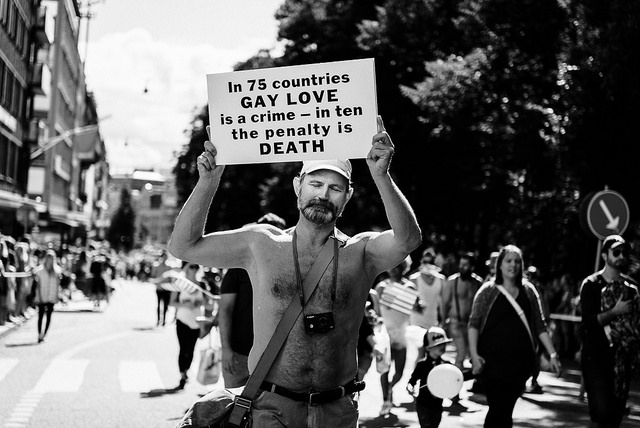 Photo of a man marching holding the sign "In 75 countries Gay Love is a crime - in ten the penalty is Death."